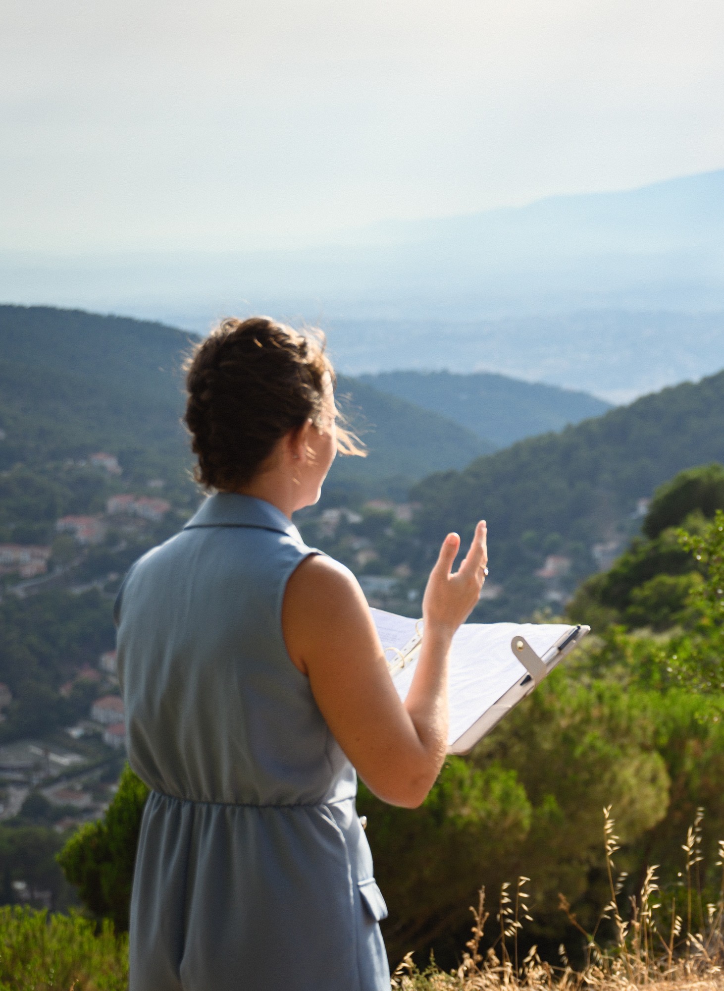 Wedding celebrant reading from a clipboard with a mountain valley view behind her